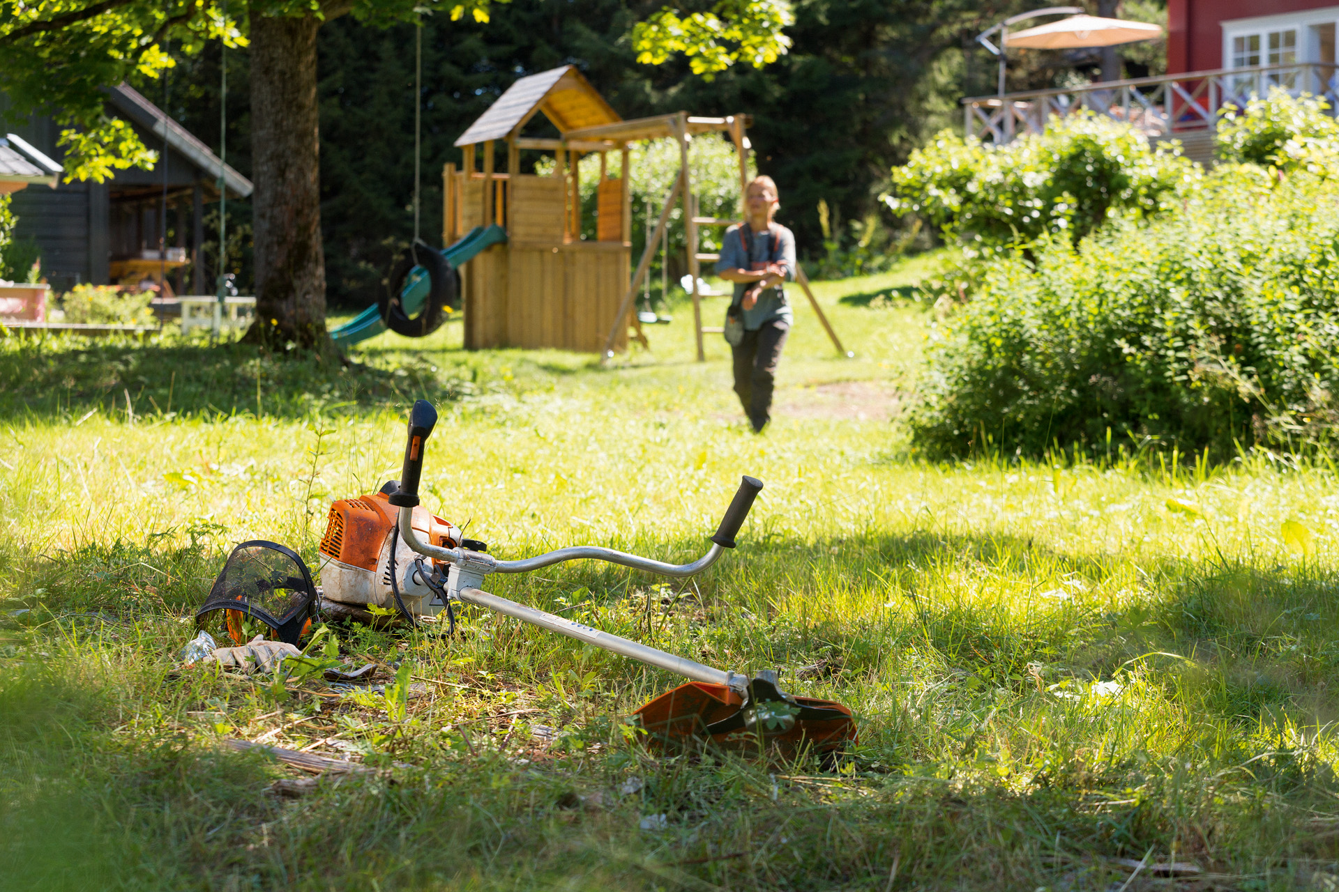 Косата за грмушки STIHL FS 240 во трева, а во позадина маж се подготвува за одржување.