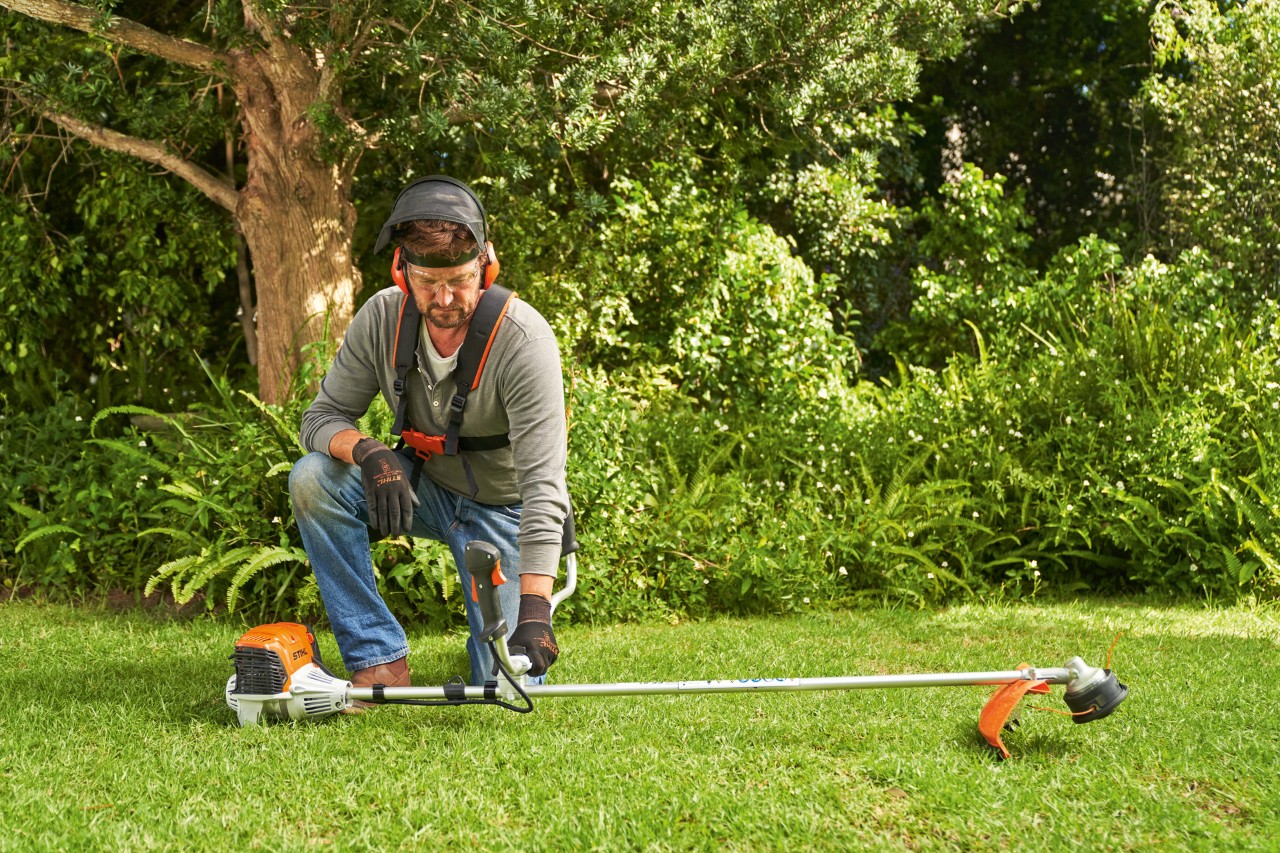 Човек става бензинска коса за грмушки STIHL FS 91 на земја за да ја запали