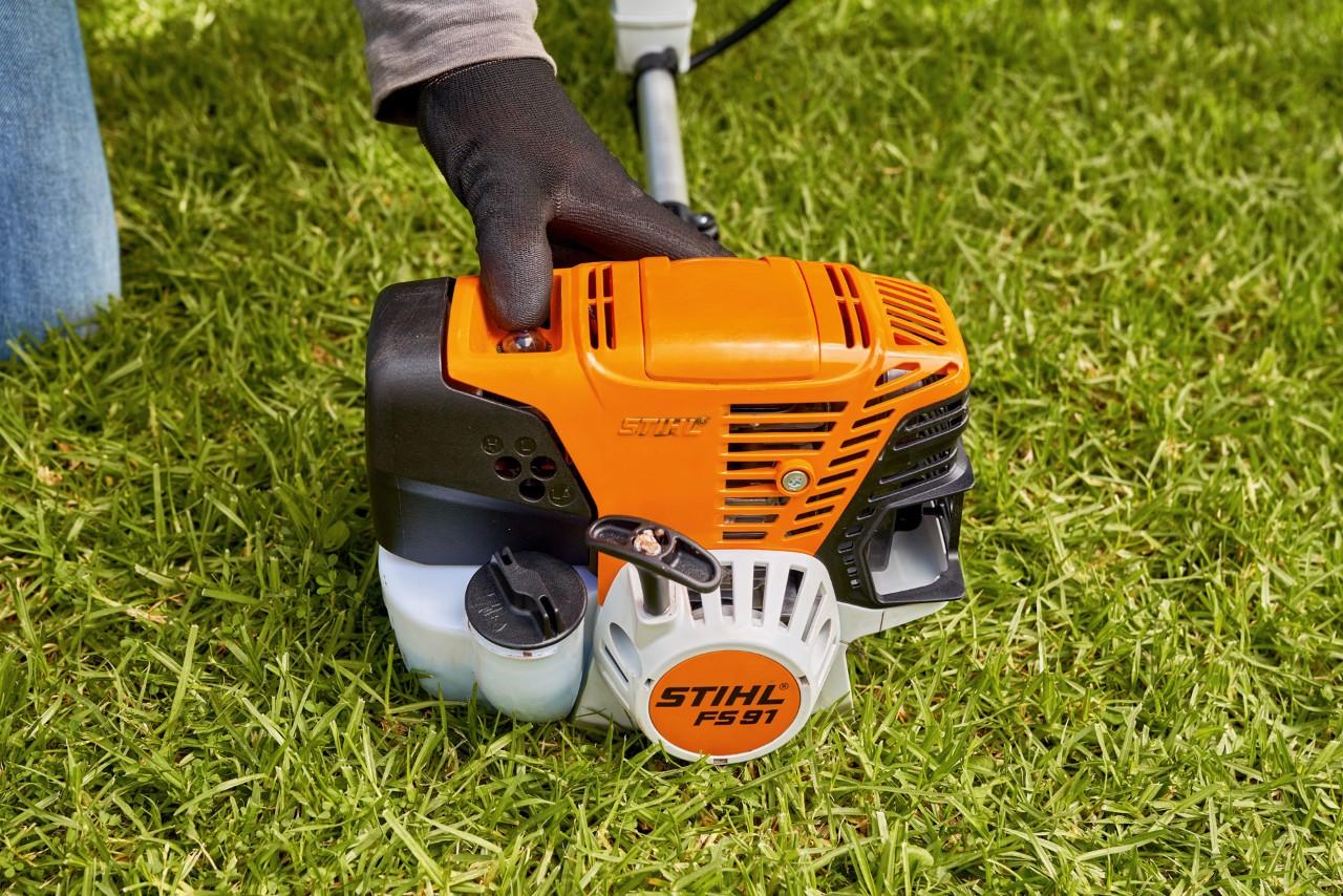 Човек притиска на пумпата за гориво на бензинска коса за грмушки STIHL FS 91 за да ја запали