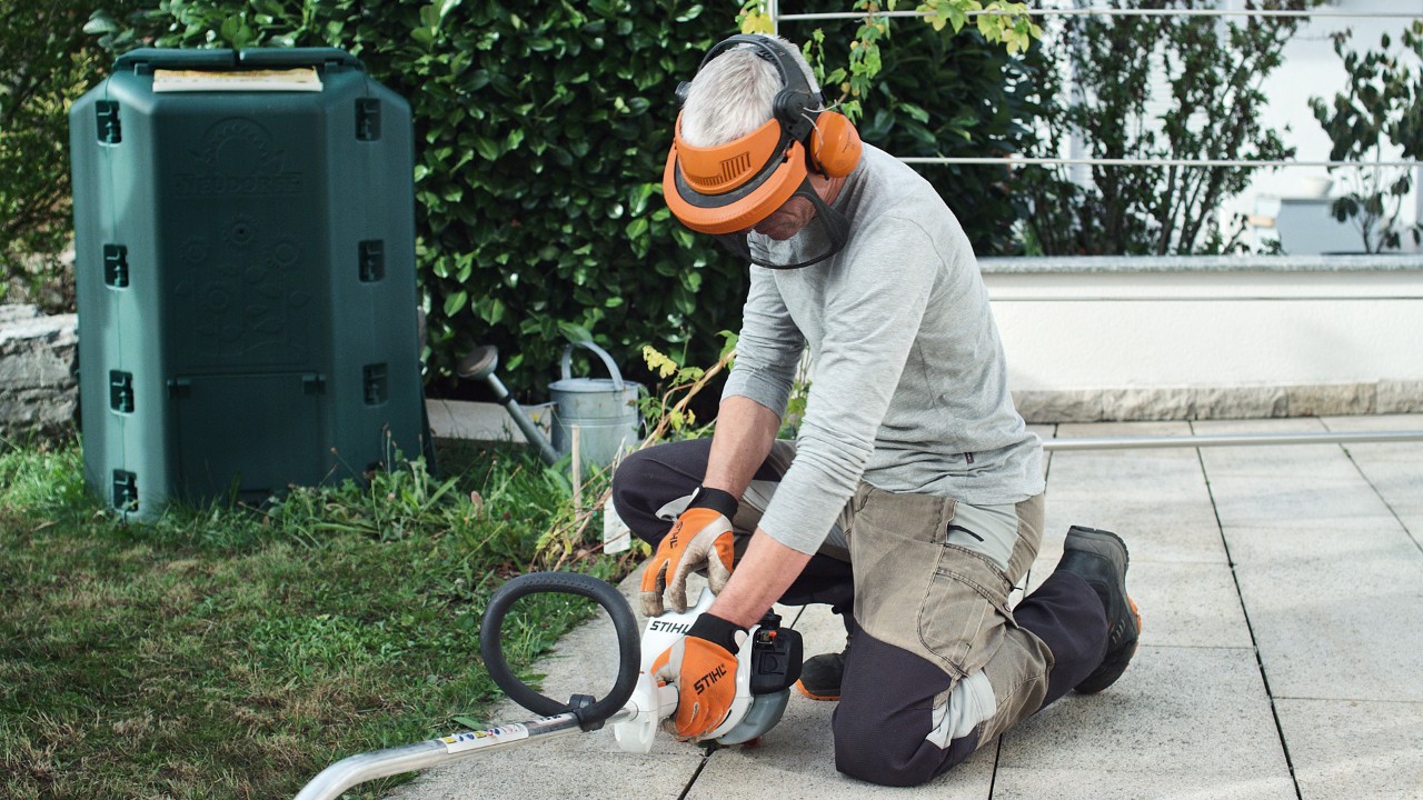 Бензинска косилка за жбунови STIHL FS 38 е притисната на земја од страна на лице кое носи заштитна облека.