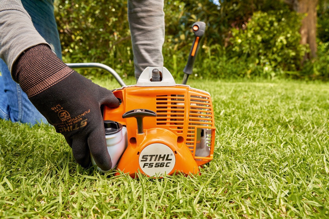 Човек притиска на пумпата за гориво на бензинскиот тример STIHL FS 56 за да го запали