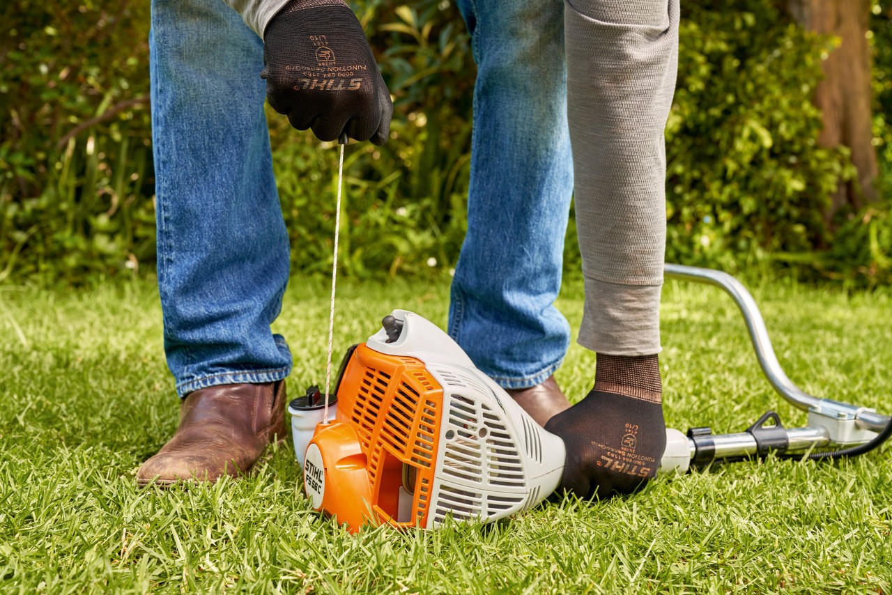 Човек го влече стартерскиот кабел на бензинскиот тример STIHL FS 56 