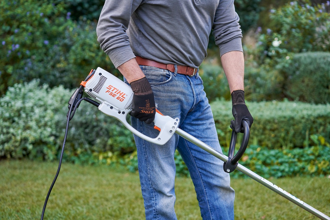 Маж со заштитни ракавици држи електрична коса за грмушки STIHL FSE 60 со двете раце