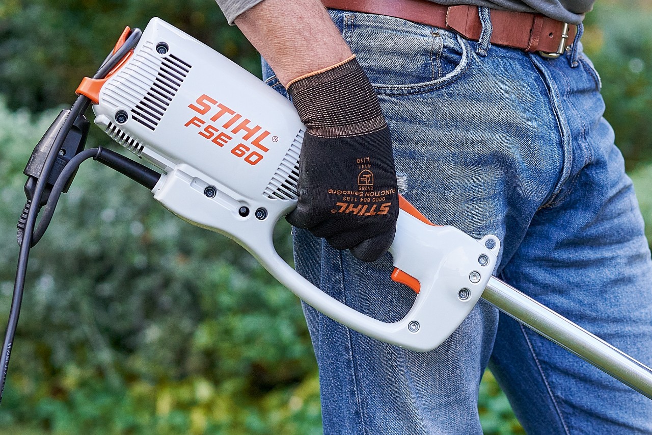 Човек притиска прекинувач за да ја исклучи електричната коса за грмушки STIHL FSE 60.