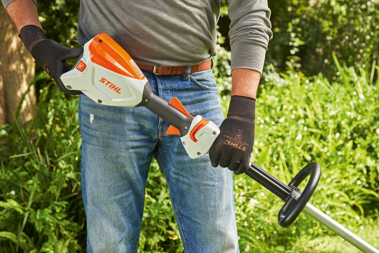 Човек со заштитни ракавици ја проверува батеријата на батерсиката коса STIHL FSA 60 пред да ја стартува.
