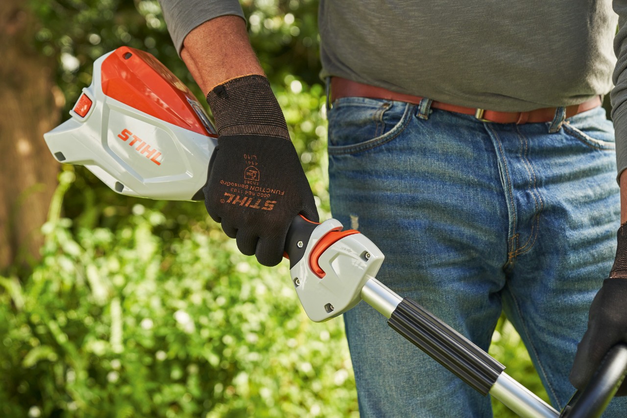 Човек со заштитни ракавици го притиска стартерот на батерсиката коса STIHL FSA 60 за да ја стартува