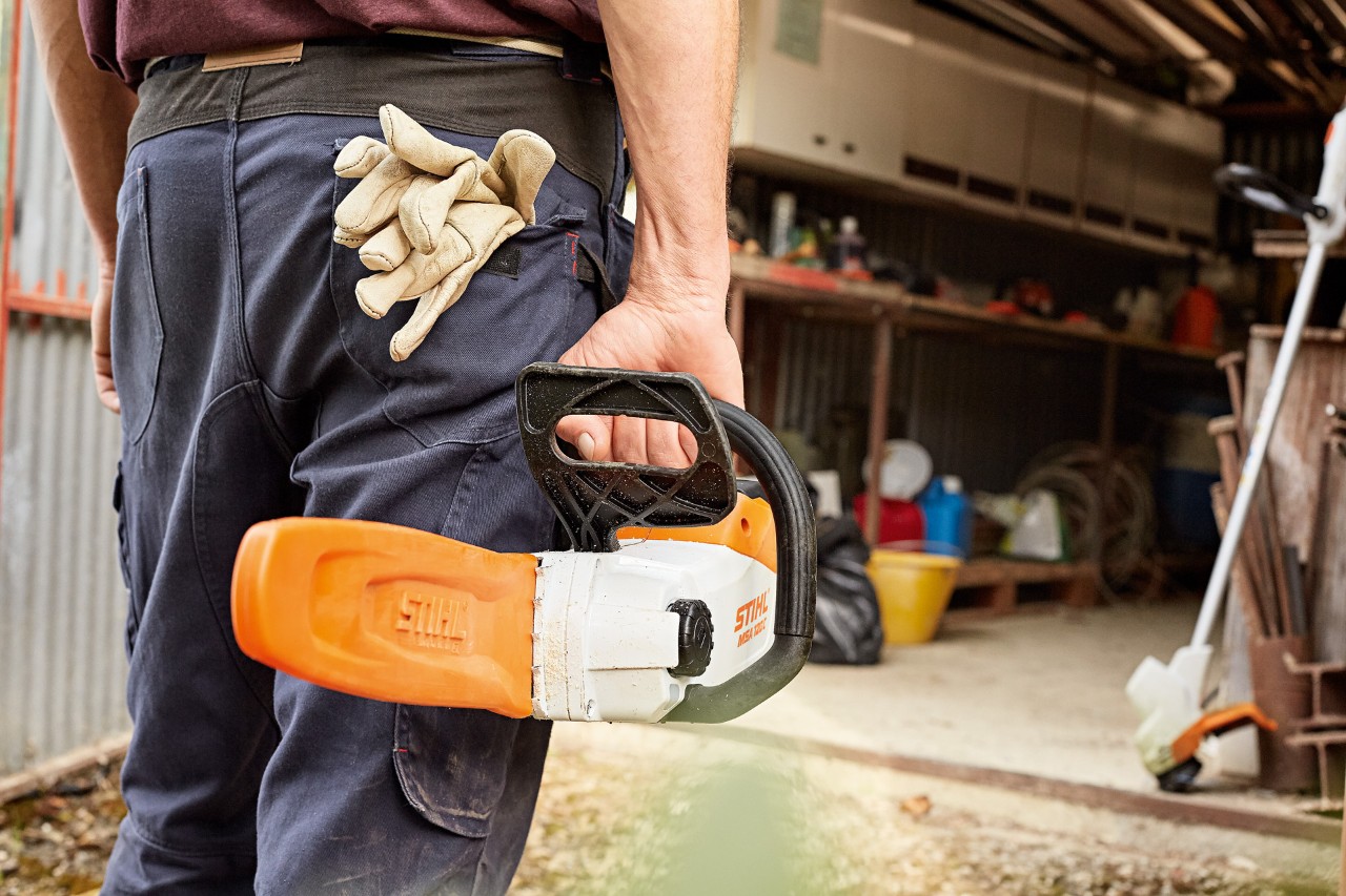 Човек влегува во работилница носејќи батериска моторна пила STIHL со футрола